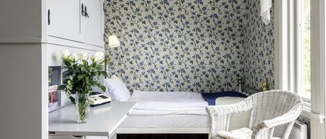 Una habitación pequeña con cama, escritorio, silla y radiador.