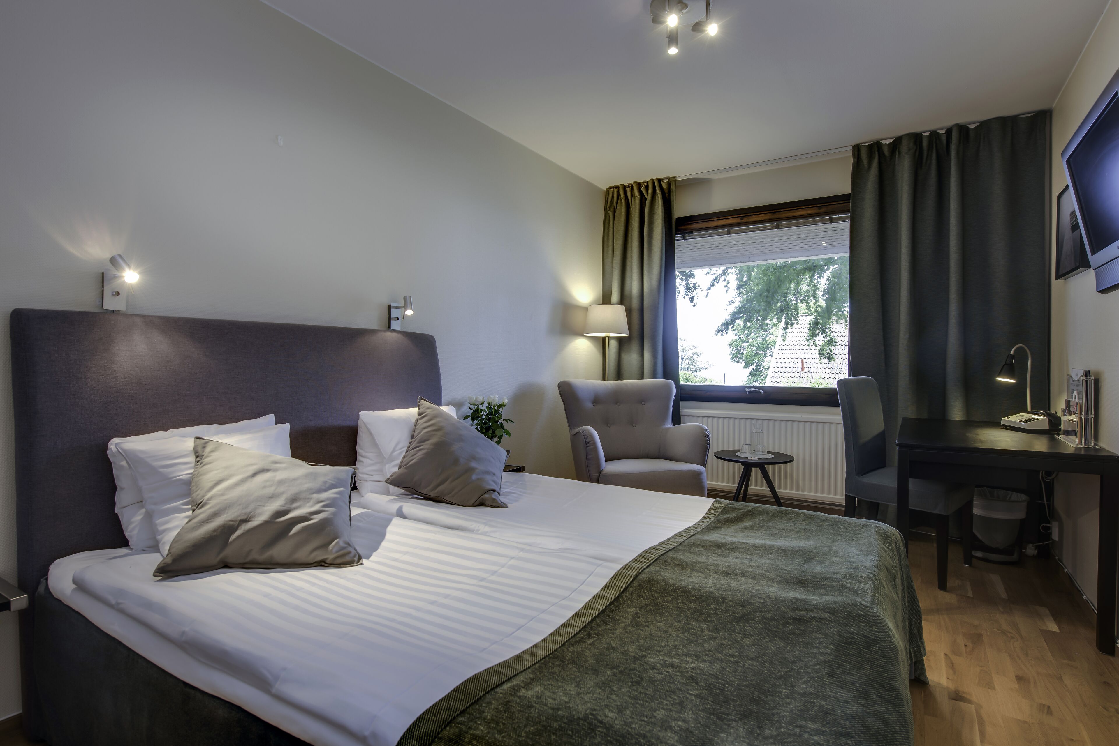 Ett hotellrum med en stor säng, ett skrivbord, en stol och utsikt över omgivningarna.