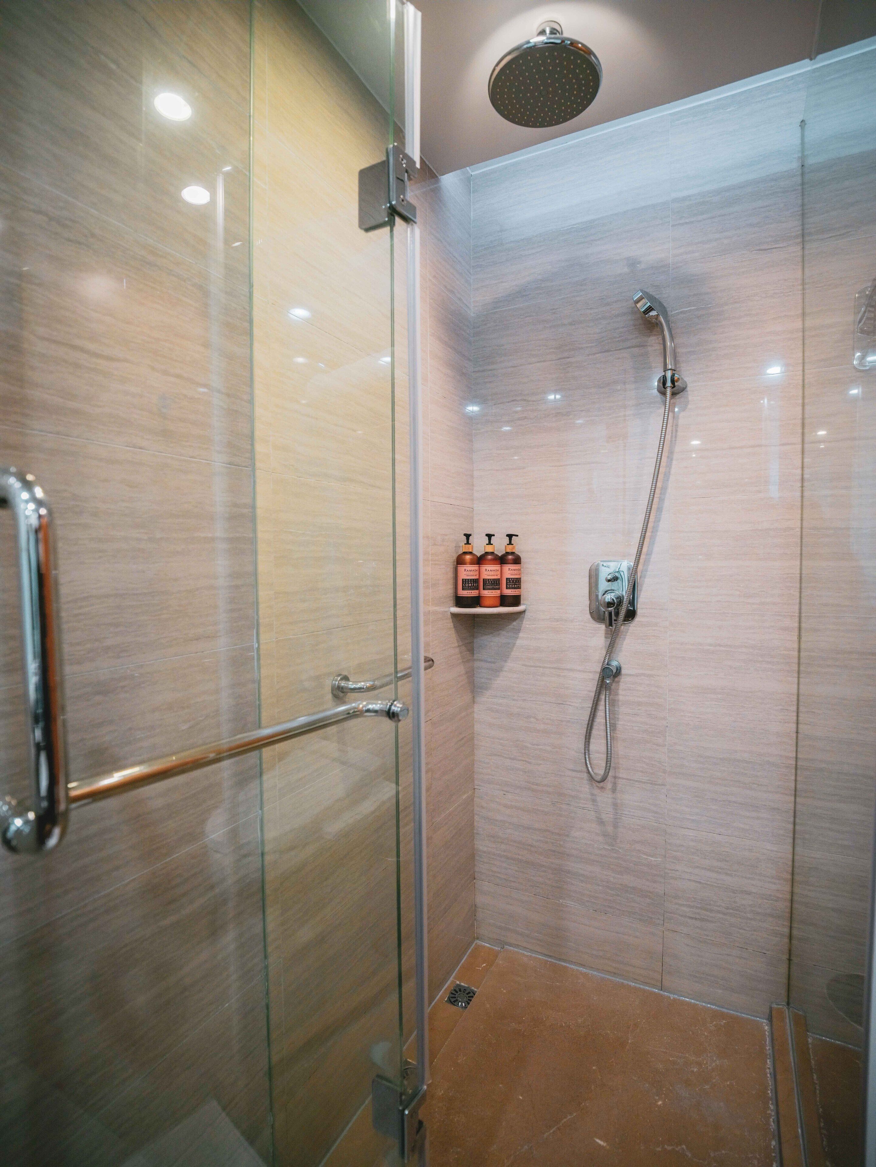 Baño con cabina de ducha acristalada, ducha de mano y panel de control en la pared.