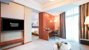 Habitación de hotel con televisión, escritorio, silla, cama y ventana con cortinas.