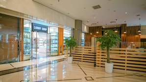 Interior moderno de un centro comercial con una tienda 'Lobby Shop', suelos de mármol pulido y zonas de estar con madera.