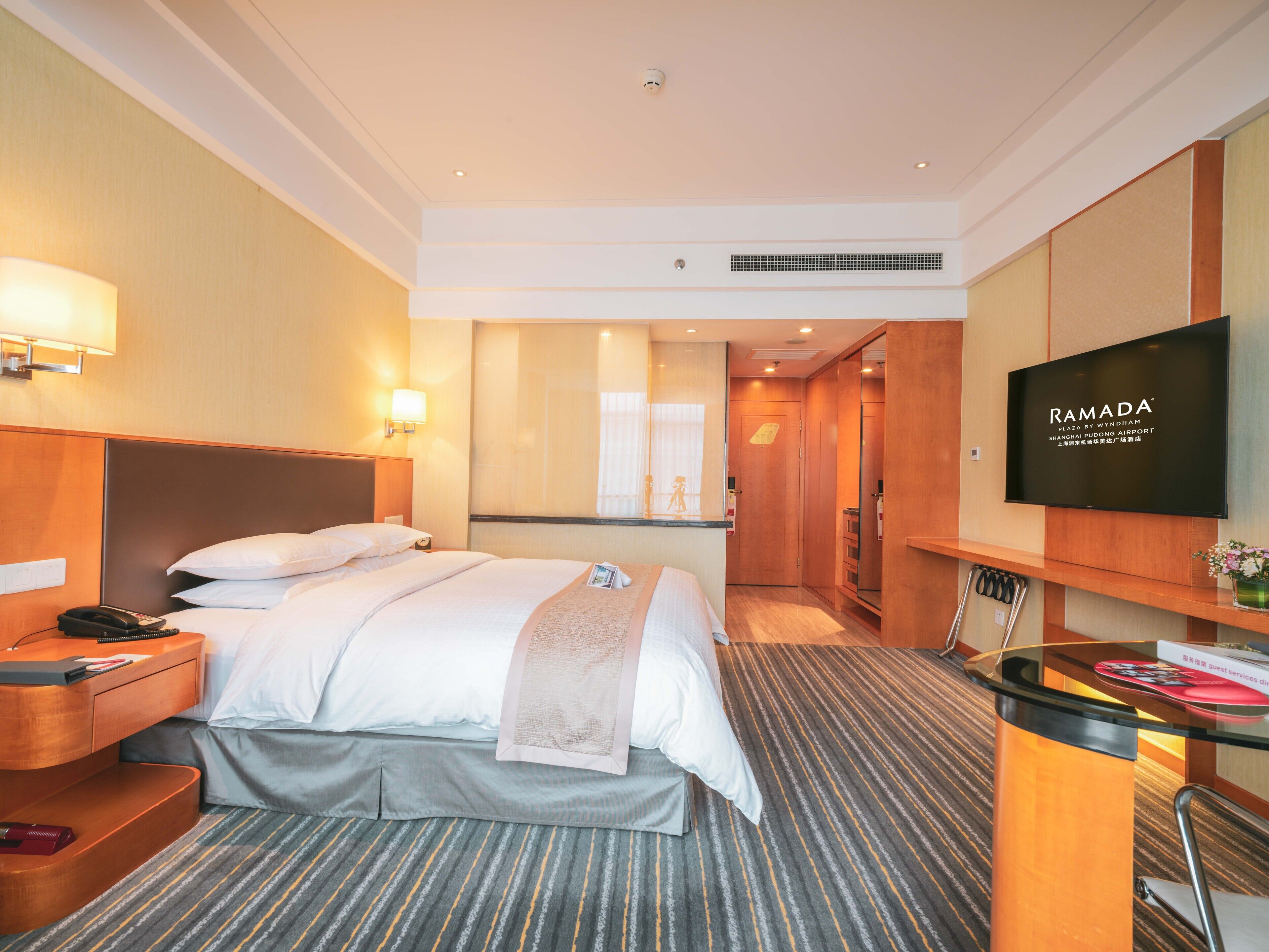 Une chambre d’hôtel avec un lit, une table de chevet, une lampe, une télévision et un miroir.