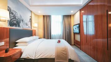 A hotel room with a bed, a desk, a TV, and a painting on the wall.