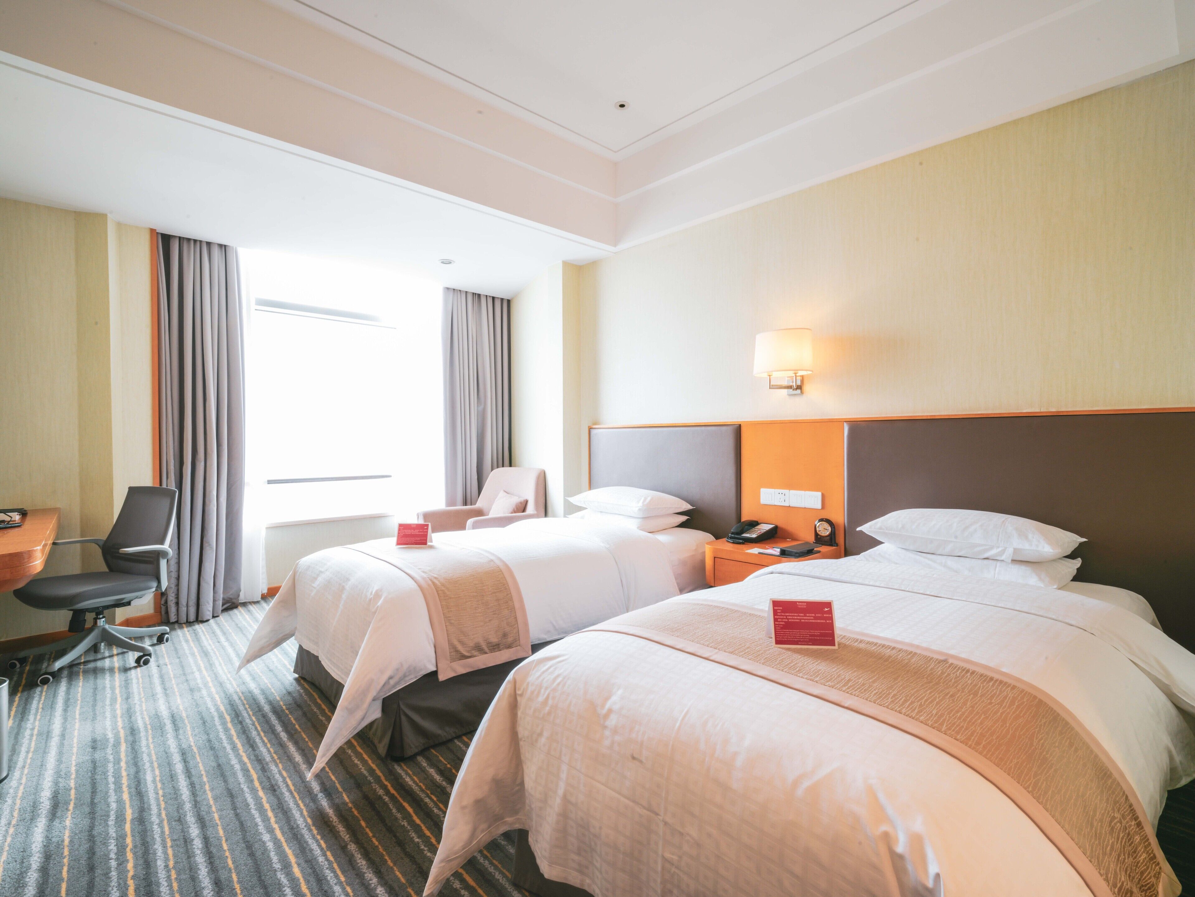 A hotel room with two beds, a desk, a chair, and a window with curtains.