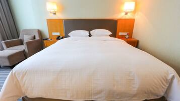 A hotel room with a large bed, two bedside lamps, a chair, a nightstand with a phone, and a clock.
