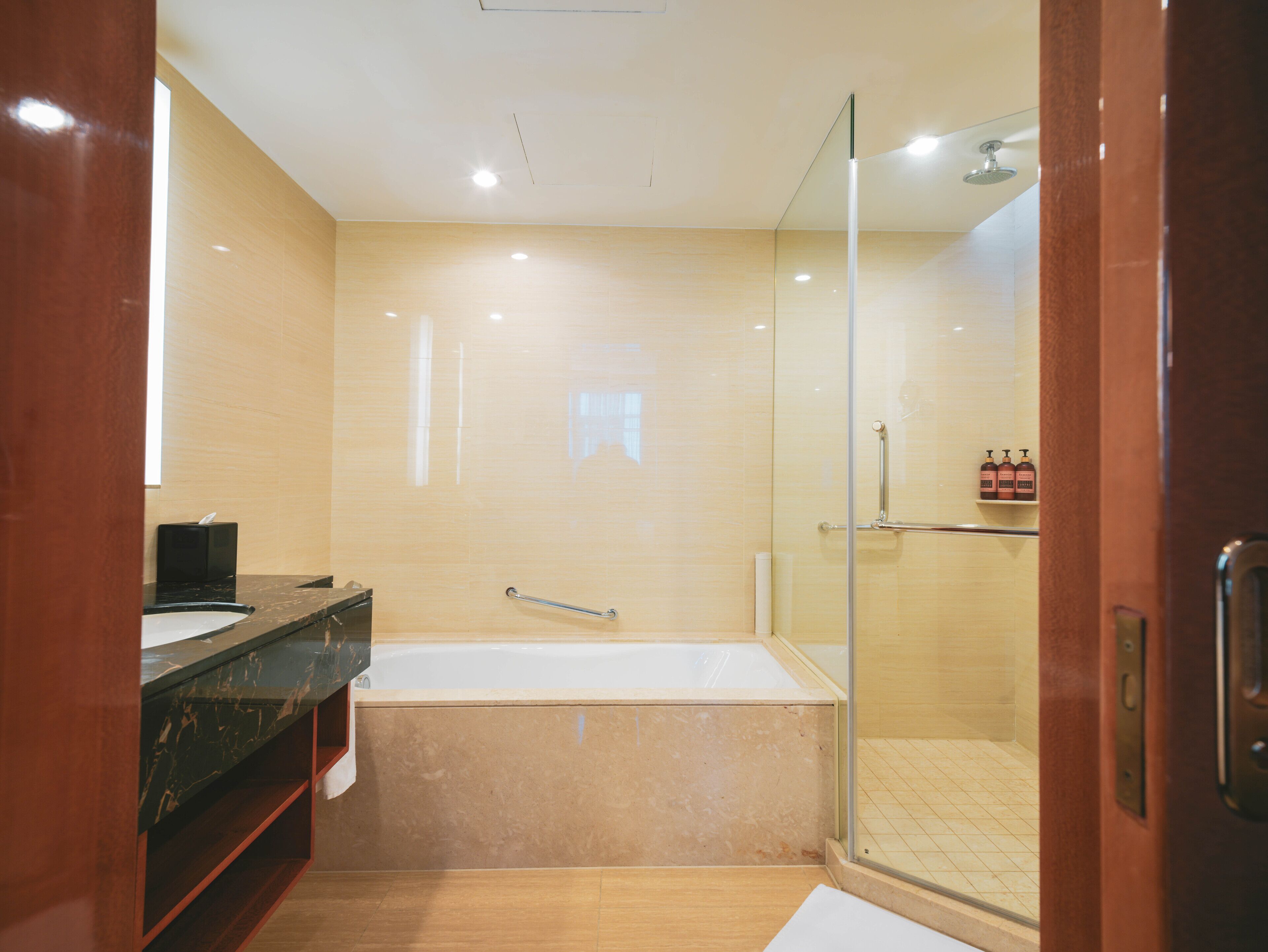 A modern bathroom with a glass-enclosed shower, a marble bathtub, and a dark marble vanity.