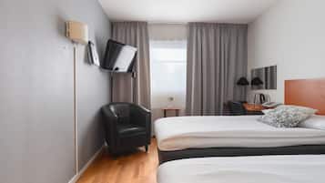 Een hotelkamer met twee bedden, een bureau, een stoel, een aan de muur bevestigde televisie en een raam met gordijnen.