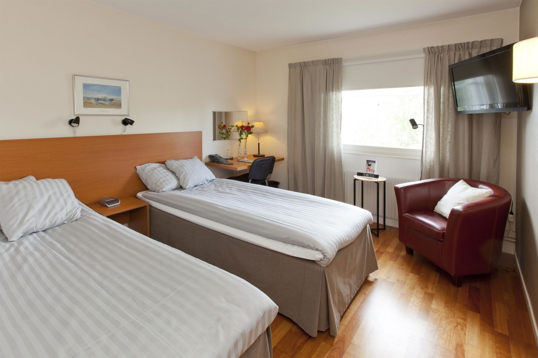 A hotel room with two beds, a desk, a chair, a TV, and a window with curtains.