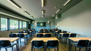 A classroom with rows of desks and chairs, a projector screen, and a window with a view of trees.