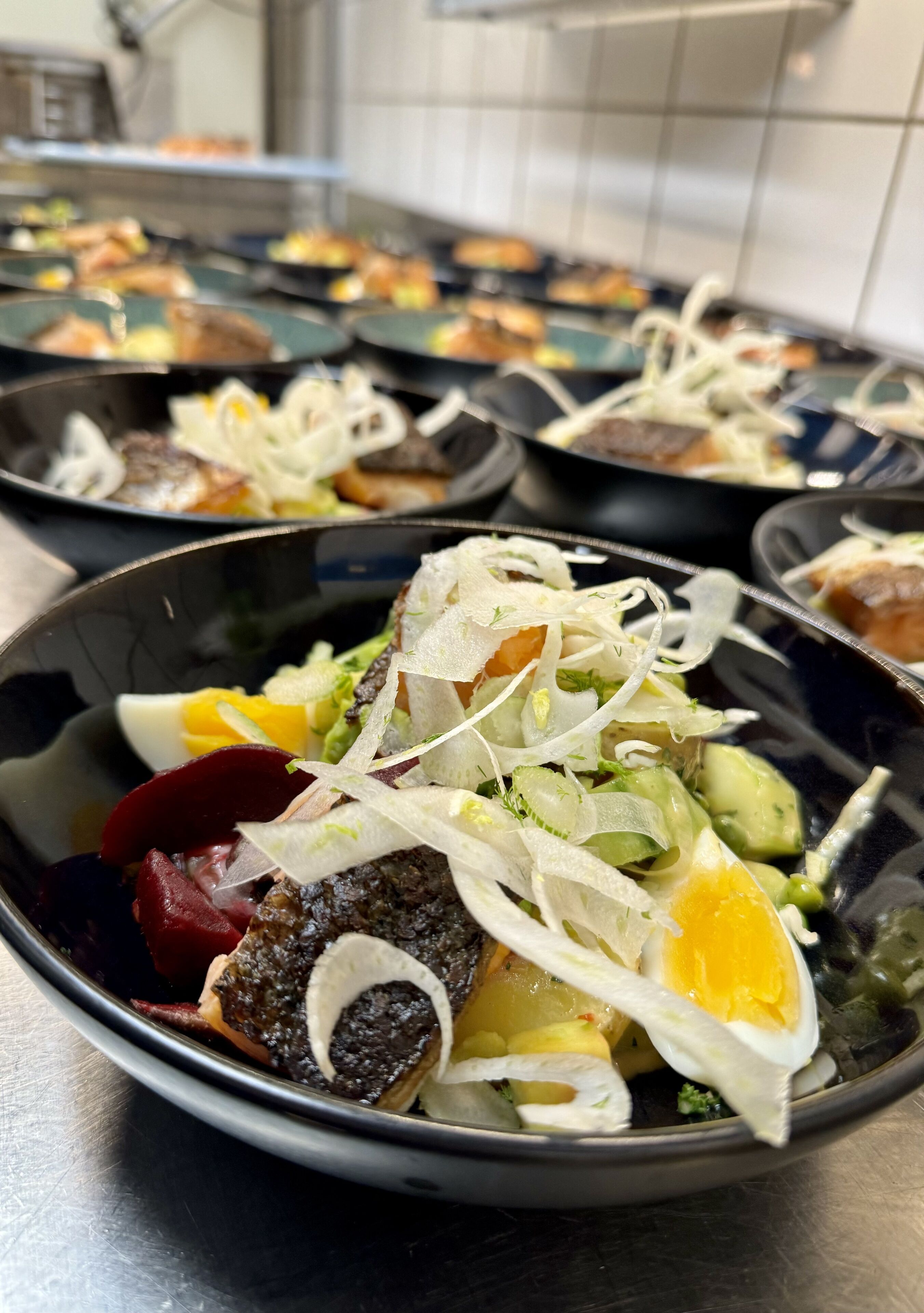 Diversos pratos em tabuleiros pretos, incluindo uma salada com ovo, beterraba e folhas verdes.