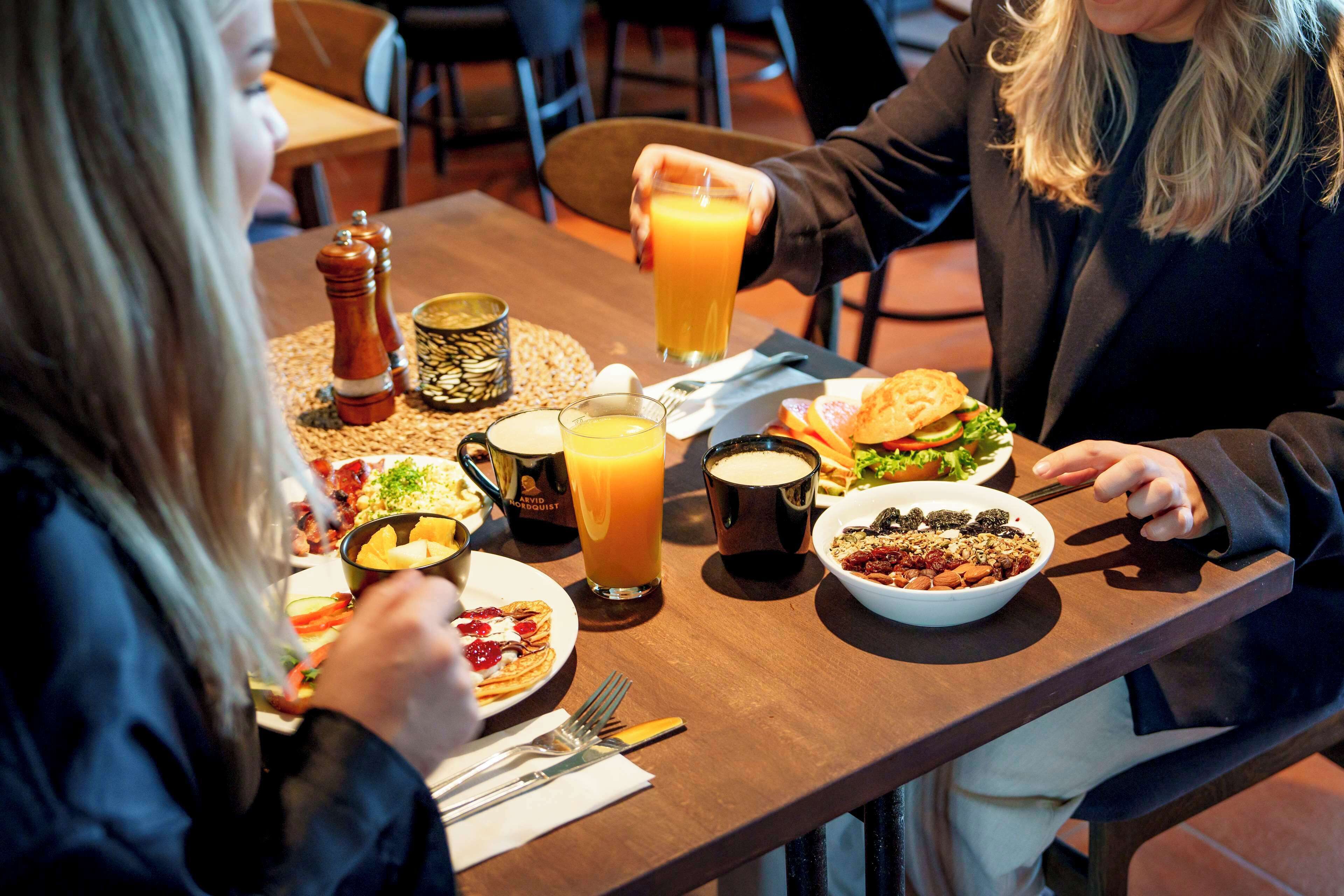 A dining table with various dishes, including a burger, salad, and a bowl of fruit. There are also condiments, a glass of orange juice, and a coffee cup.