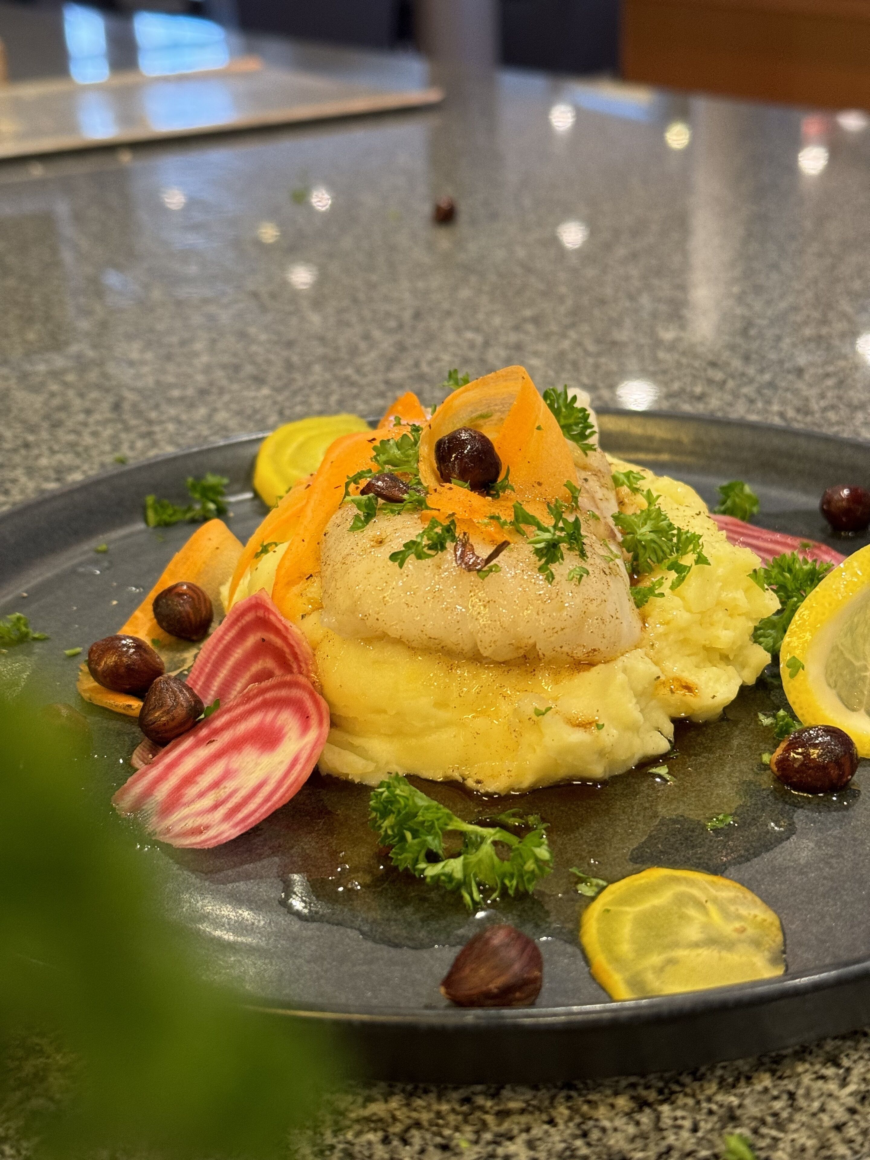 En upplagd rätt med en fiskfilé, potatismos och garnering.