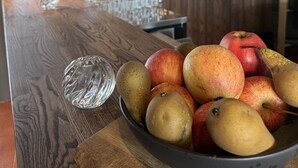 A bar area with a wooden counter, a bowl of fruit, and hanging glasses.
