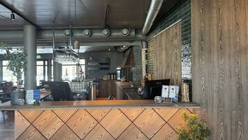 A reception area with a wooden reception desk, a potted plant, and a view of the bar area with a brick wall.