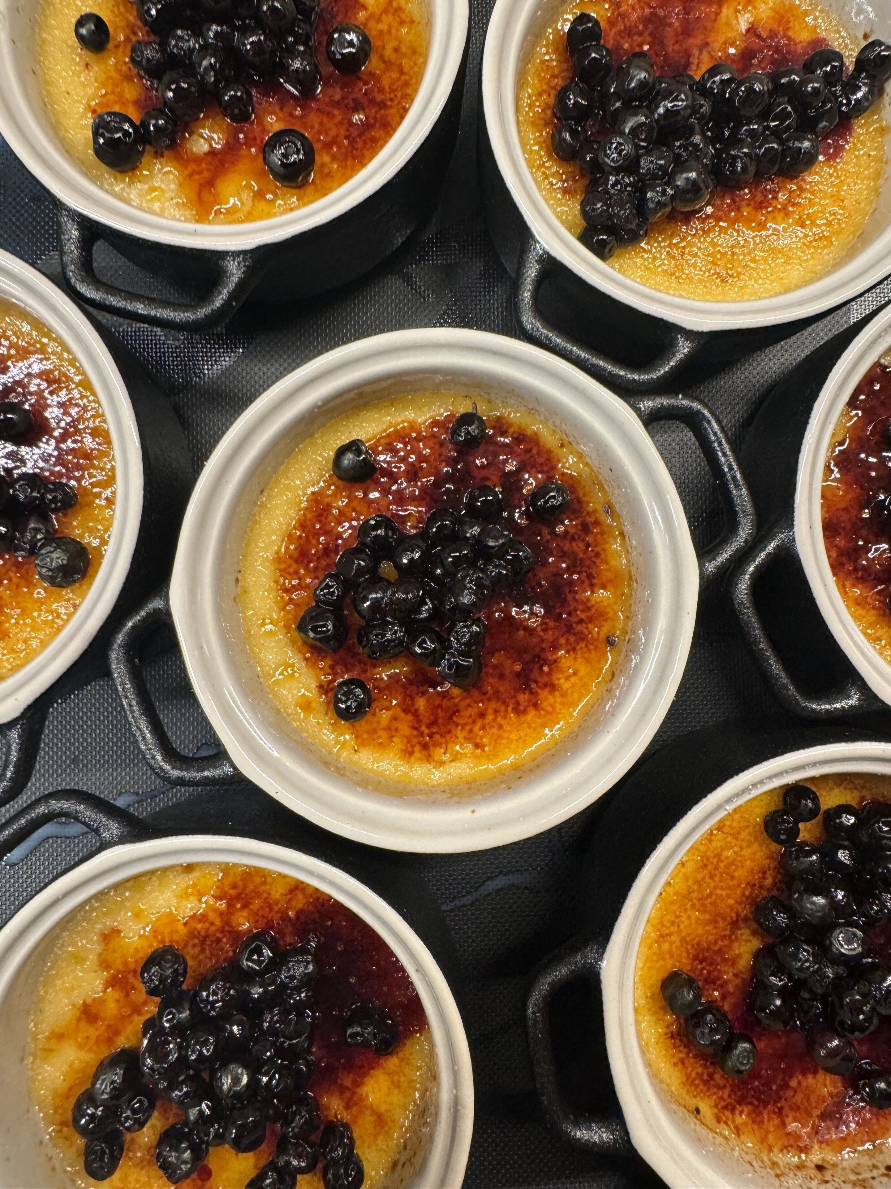 Multiple ramekins of crème brûlée arranged on a black tray.