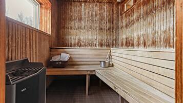 A sauna room with wooden walls, a bench, a trash bin, and a window.