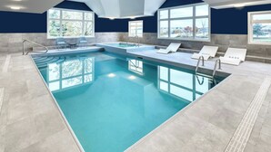 Una gran piscina cubierta con agua cristalina, rodeada de sillones de descanso y vistas al exterior a través de amplios ventanales.