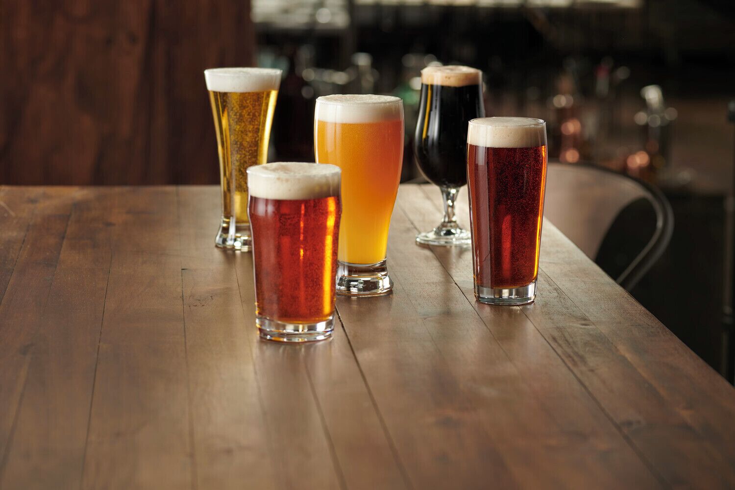 A wooden table with five glasses of beer.
