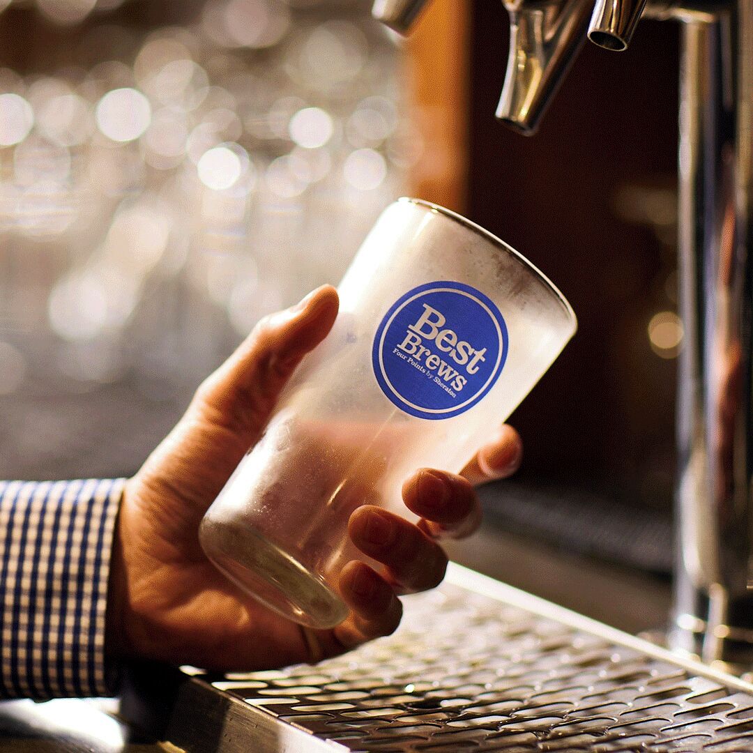 A hand holding a glass with a logo, near a tap.