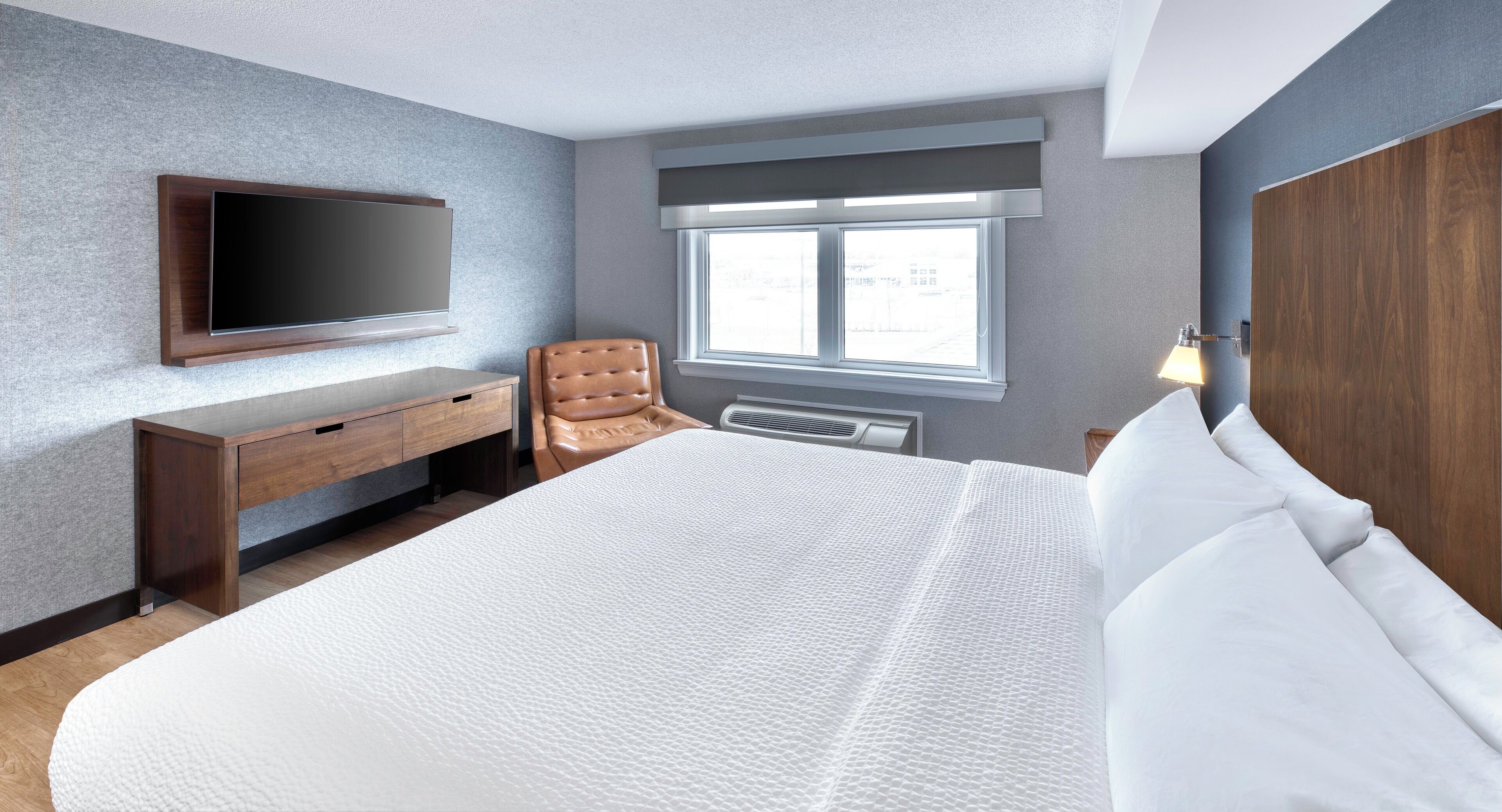 Une chambre d’hôtel moderne dotée d’un grand lit, d’un bureau, d’une chaise, d’un téléviseur à écran plat fixé au mur et d’une fenêtre laissant entrer la lumière naturelle.