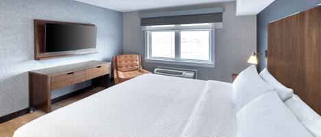 Une chambre d’hôtel moderne dotée d’un grand lit, d’un bureau, d’une chaise, d’un téléviseur à écran plat fixé au mur et d’une fenêtre laissant entrer la lumière naturelle.