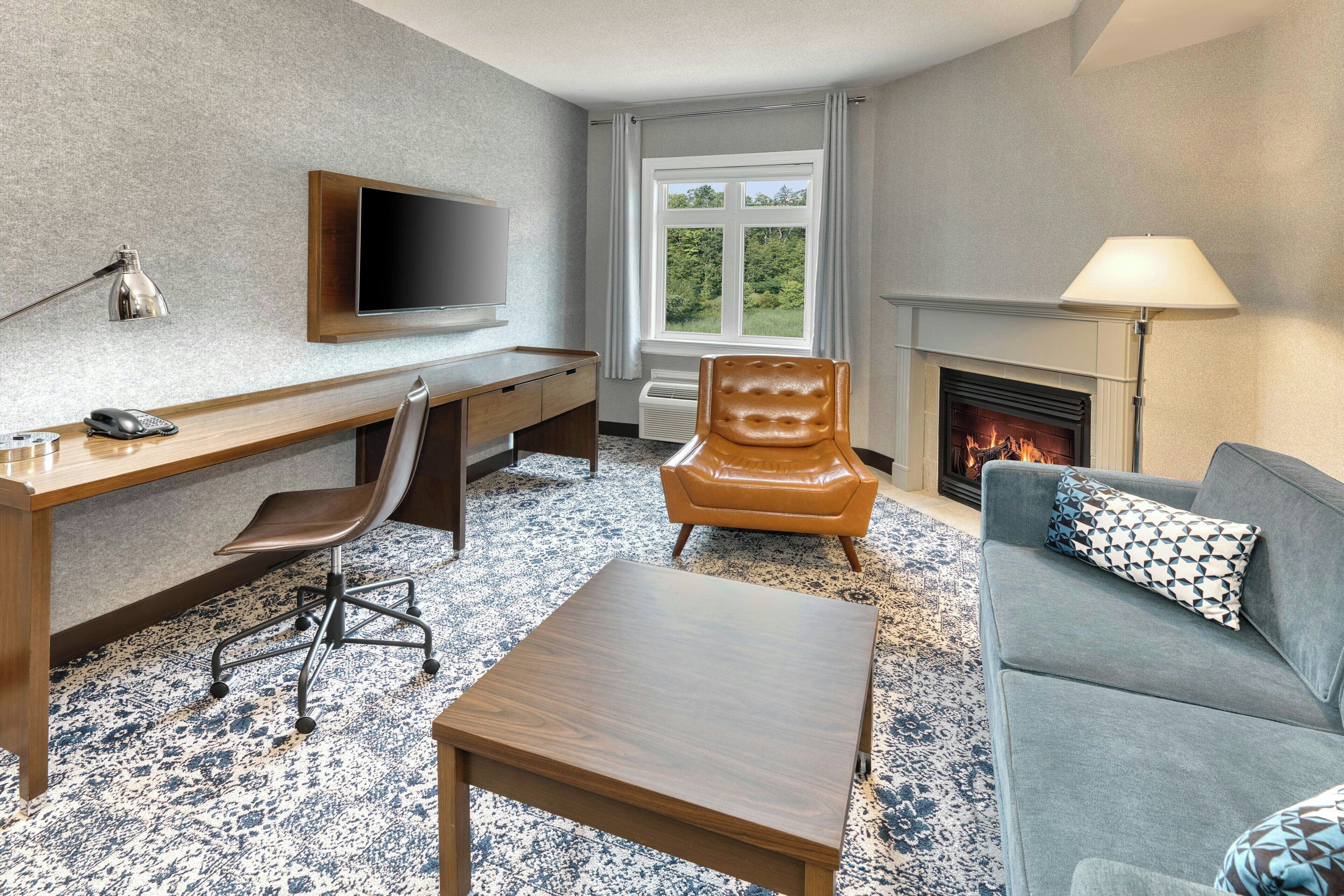 A modern living room with a wooden desk, leather chair, grey sofa, and a fireplace.