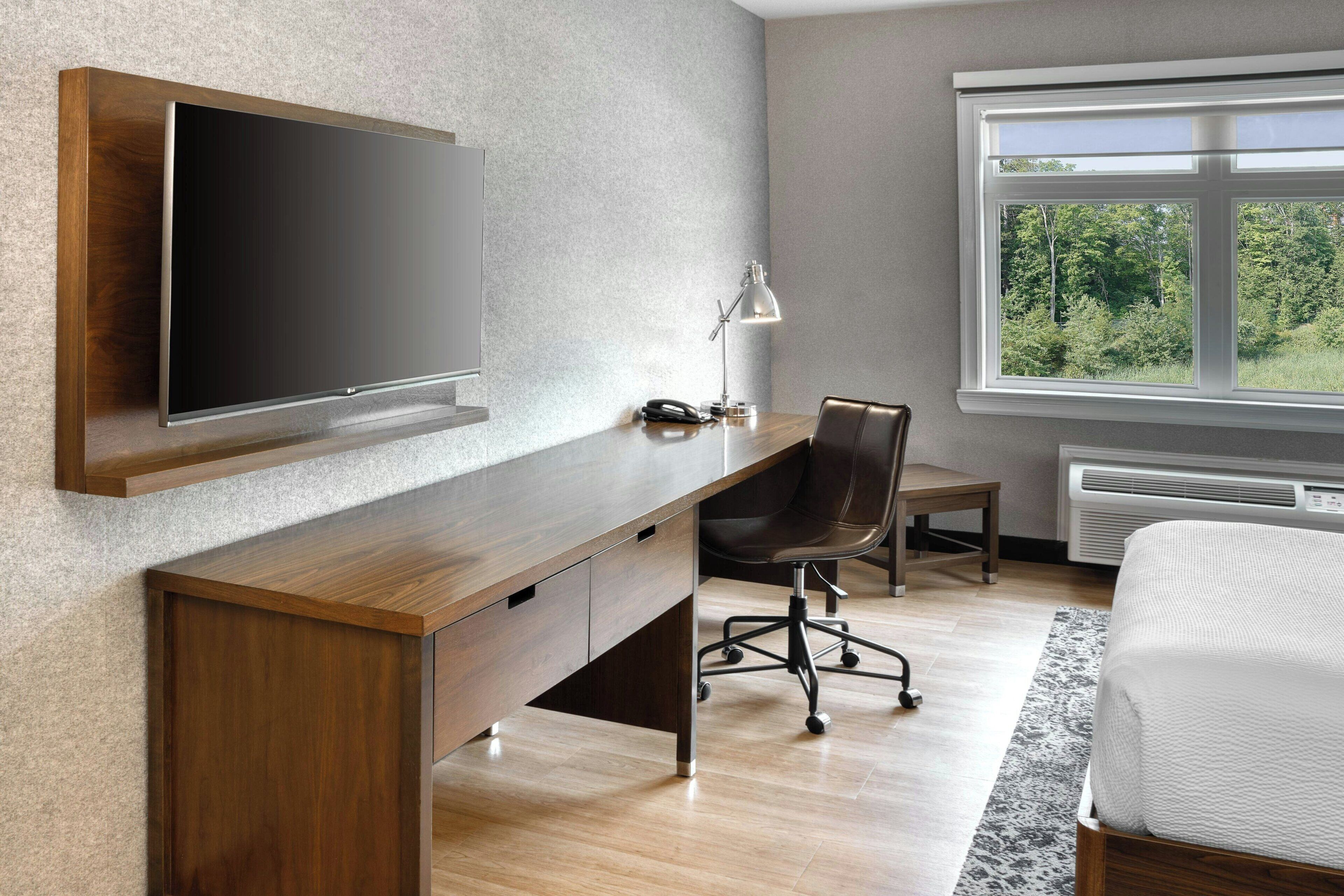 Un dormitorio moderno con un escritorio de madera, un televisor montado, una silla y una cama.