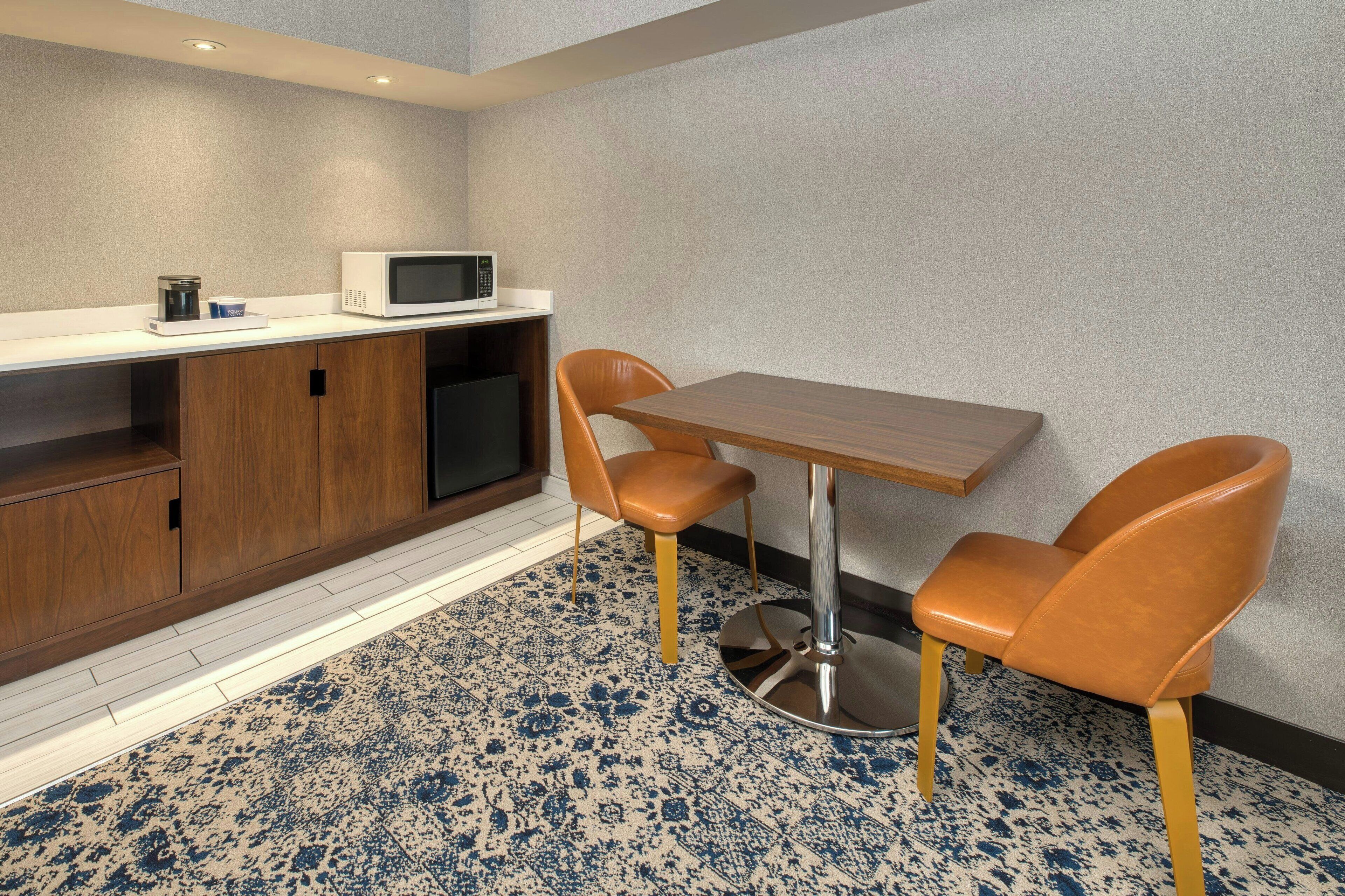 Una kitchenette compacta con microondas, cafetera y armarios de almacenamiento. Hay una mesa de madera con dos sillas y un piso con diseño.