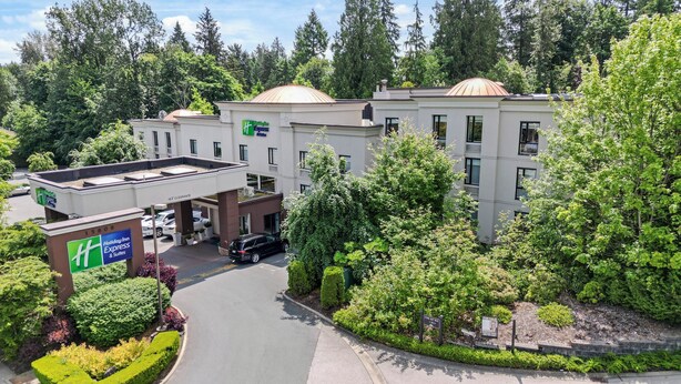 Un hotel Holiday Inn Express amb un pàrquing, envoltat de vegetació i arbres.