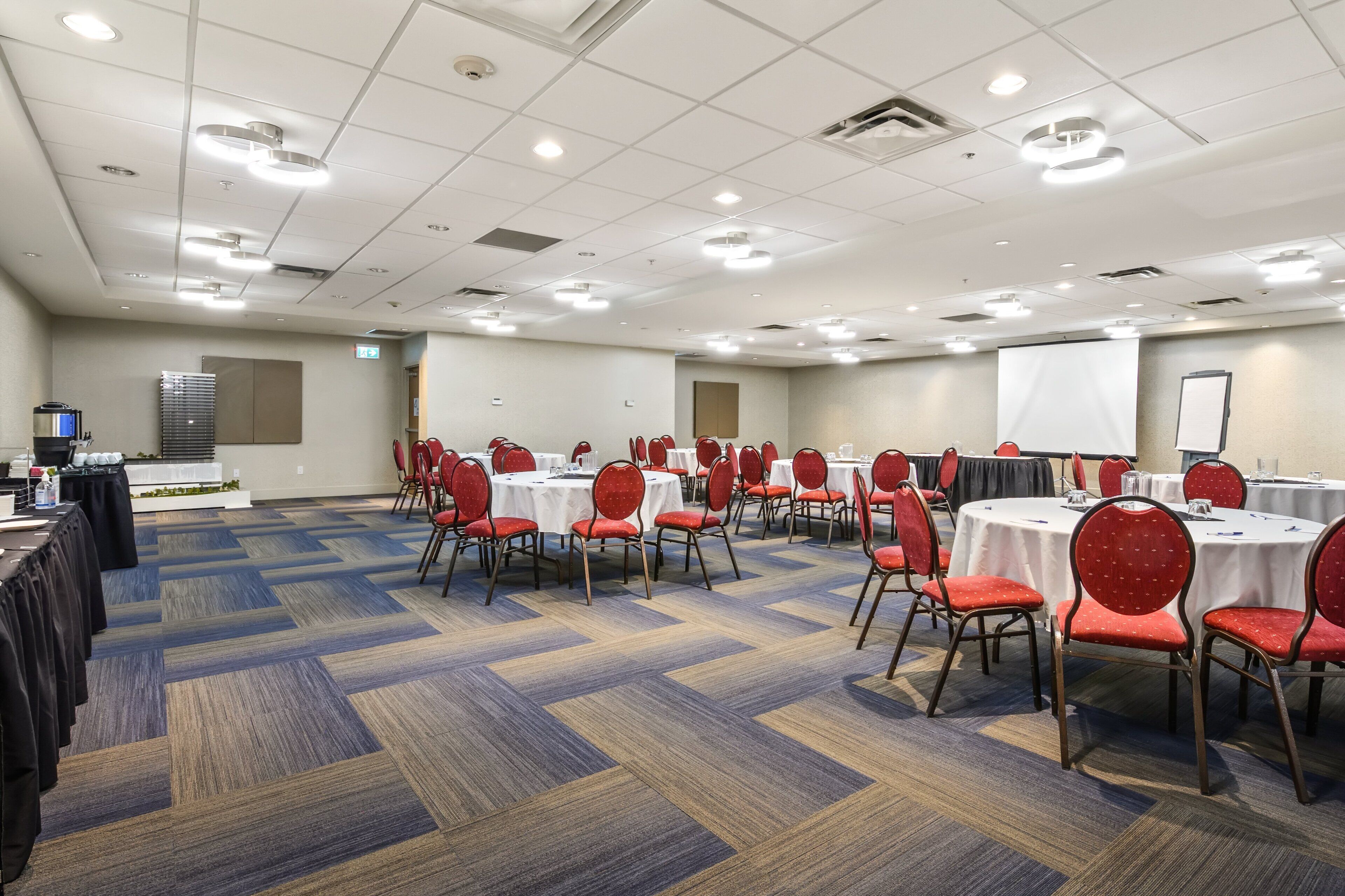 A conference room with multiple tables and chairs, carpeted flooring, and ceiling lights.