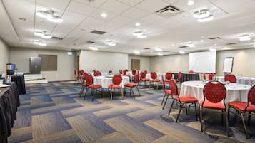A conference room with multiple tables and chairs, carpeted flooring, and ceiling lights.