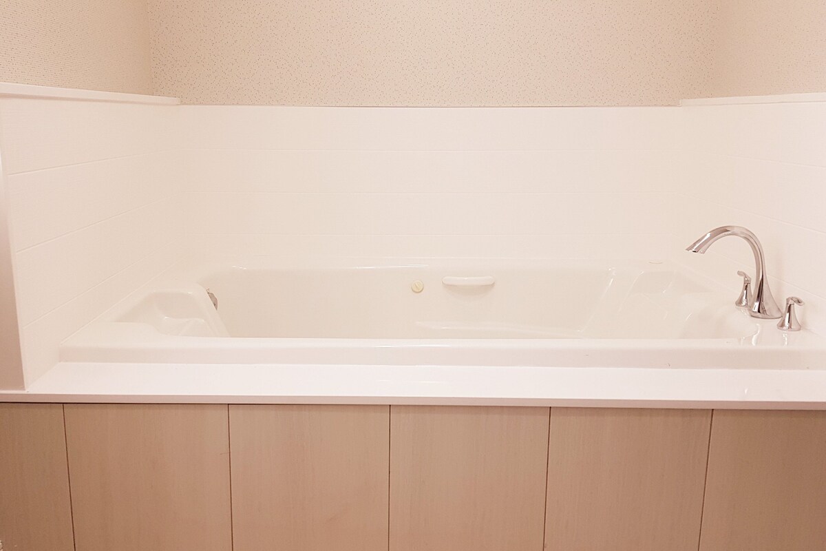 A white bathtub with a single faucet and a control knob, set against a plain wall.