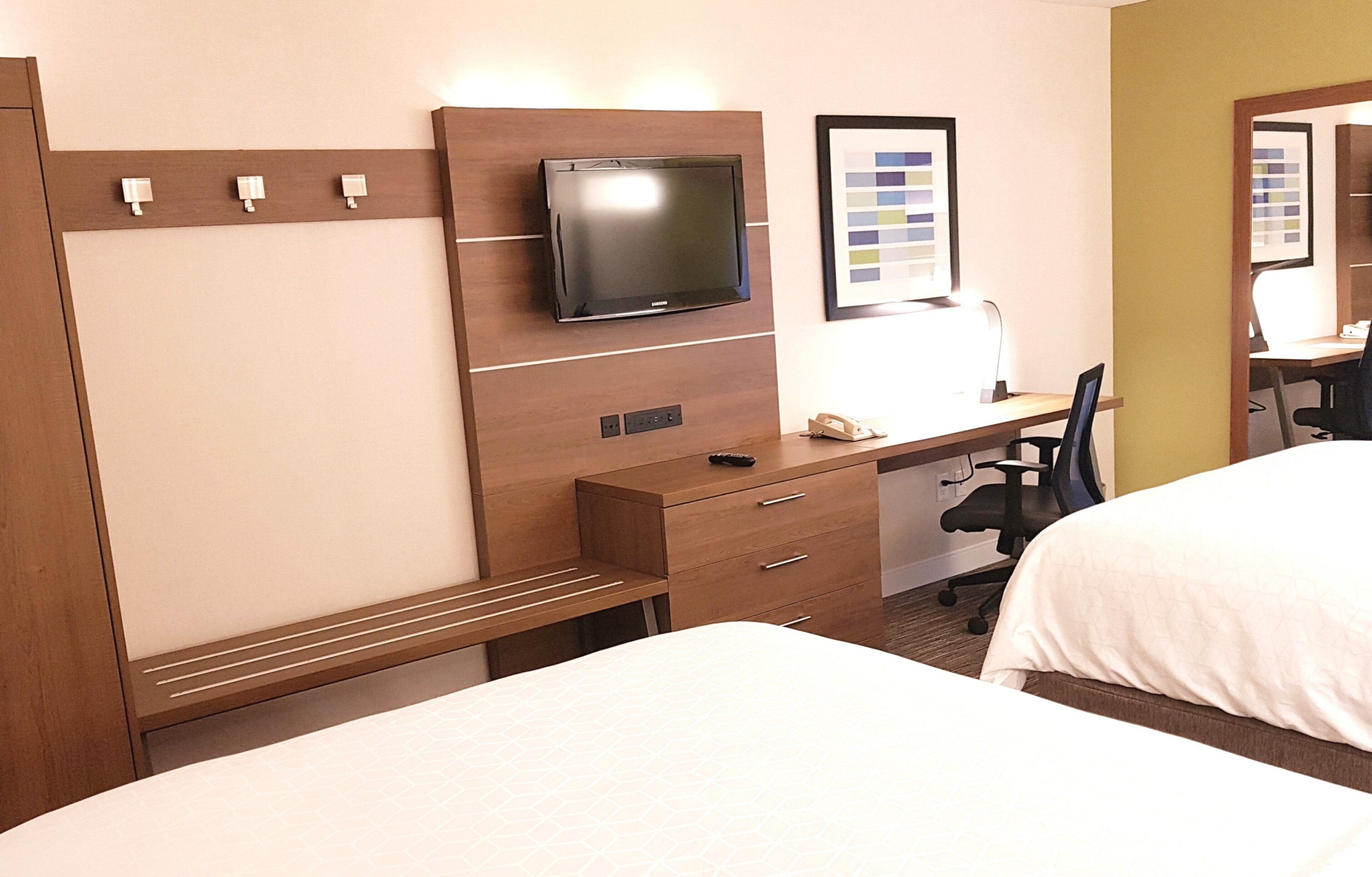 Habitación de hotel con cama, escritorio y silla, televisión e imagen enmarcada en la pared.