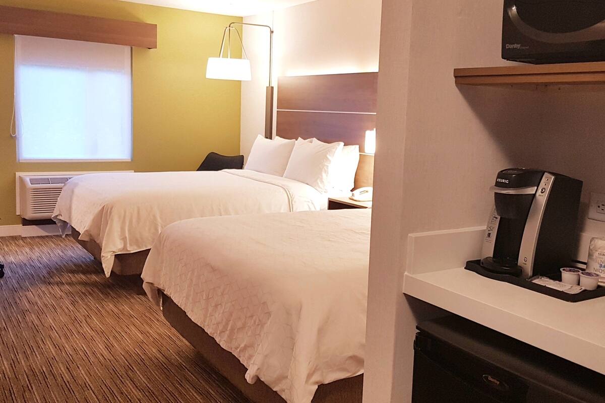 A hotel room with two beds, a minibar, a coffee maker, and a television.