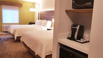 A hotel room with two beds, a minibar, a coffee maker, and a television.