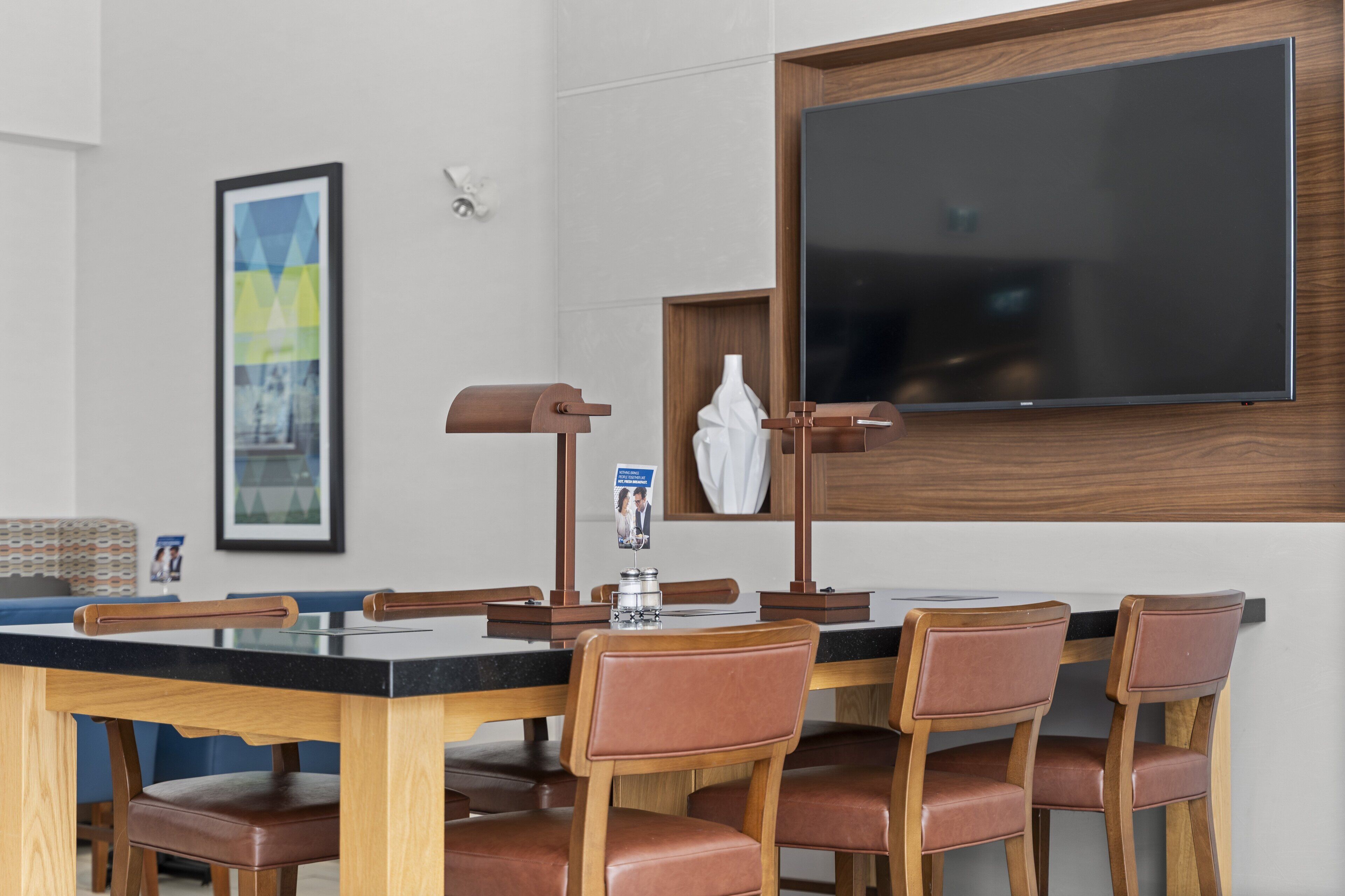 A hotel room with a wooden dining table, six brown leather chairs, a blackboard, and a framed picture on the wall.