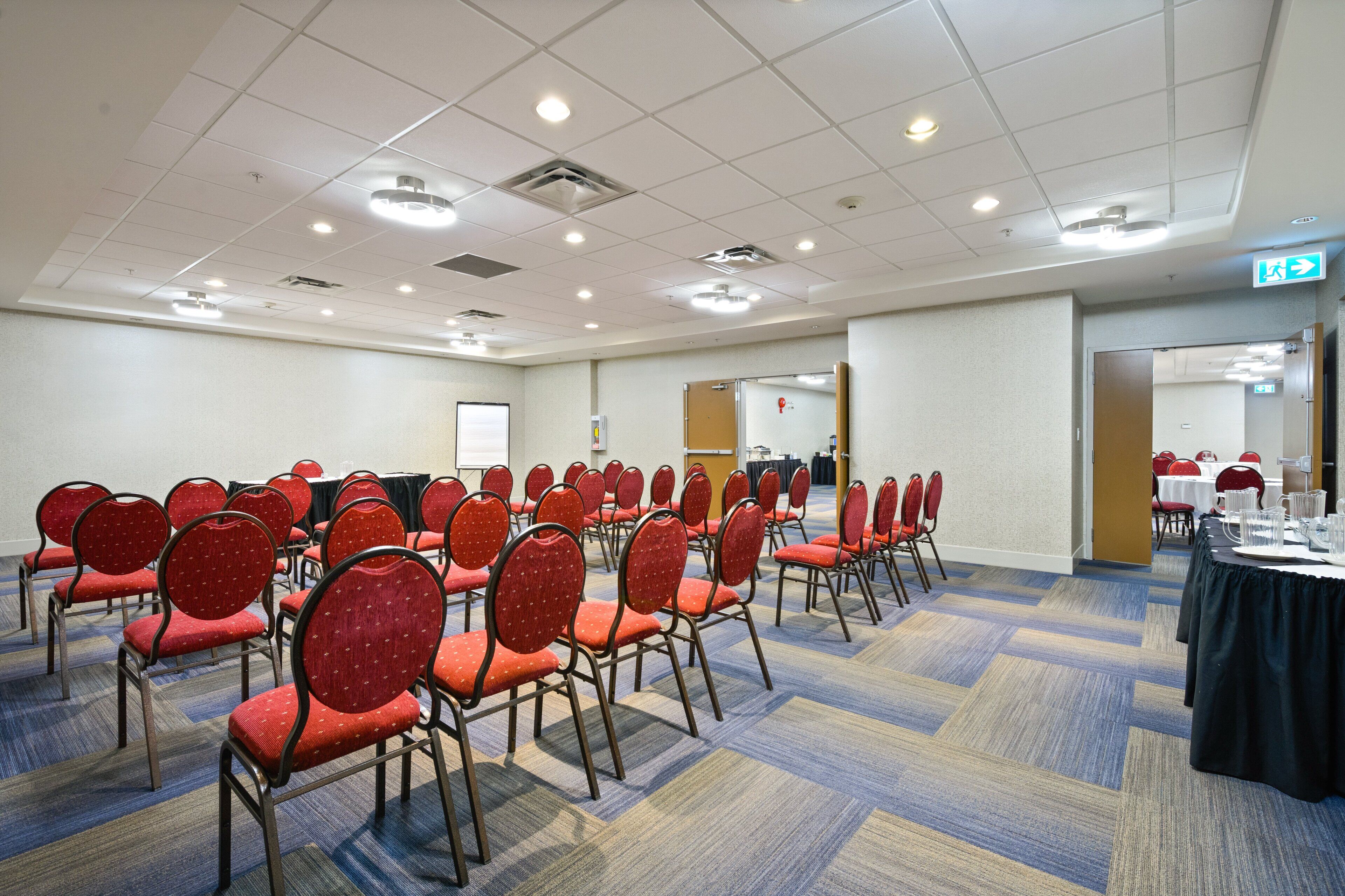 Un salón de conferencias con filas de sillas rojas, una pizarra y piso alfombrado.