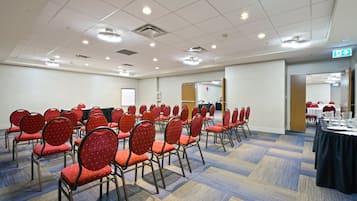 Un salón de conferencias con filas de sillas rojas, una pizarra y piso alfombrado.