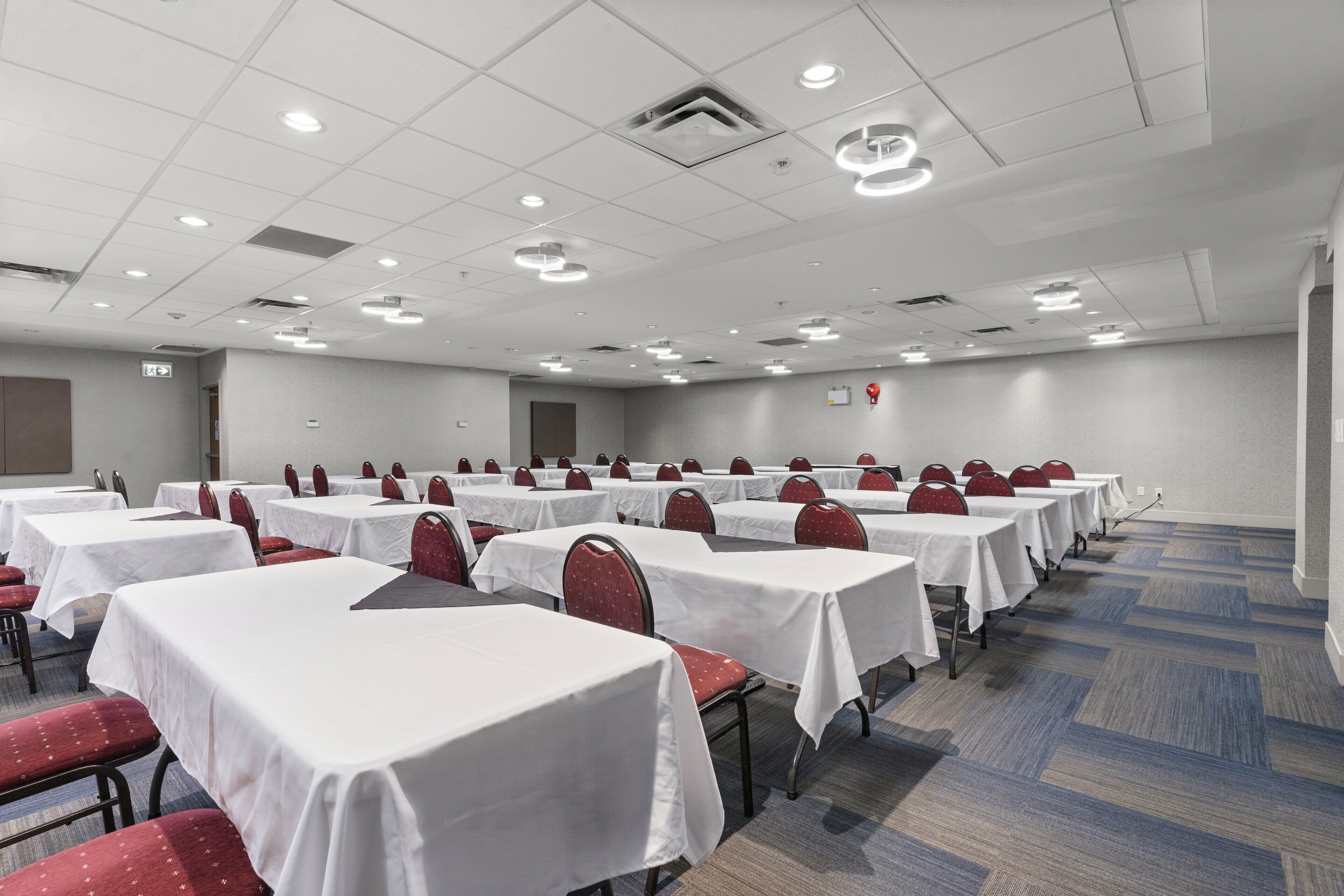 Une salle de conférence dotée de plusieurs tables et chaises, de nappes blanches et d’un sol recouvert de moquette.