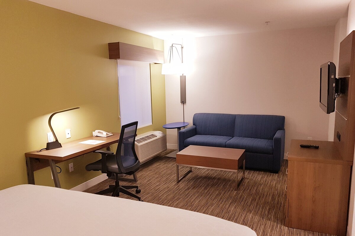 A hotel room with a bed, desk, chair, sofa, and a TV.
