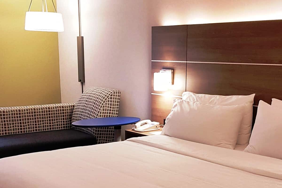 A hotel room with a bed, a sofa, a small table, a phone, and a lamp.