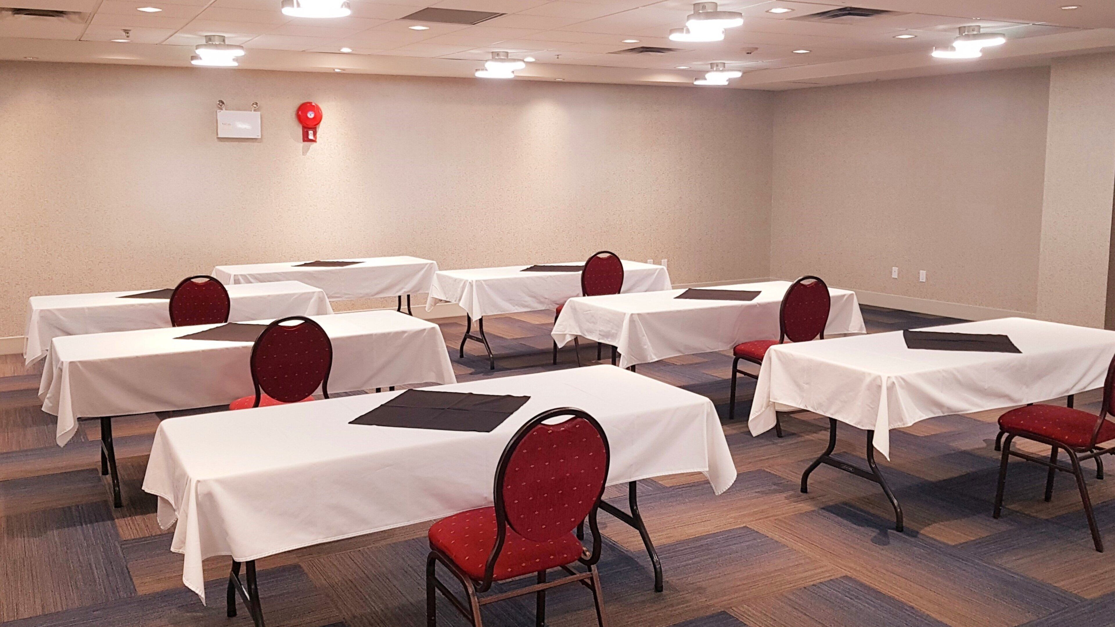 A conference room with multiple tables and chairs, white tablecloths, and red chairs.
