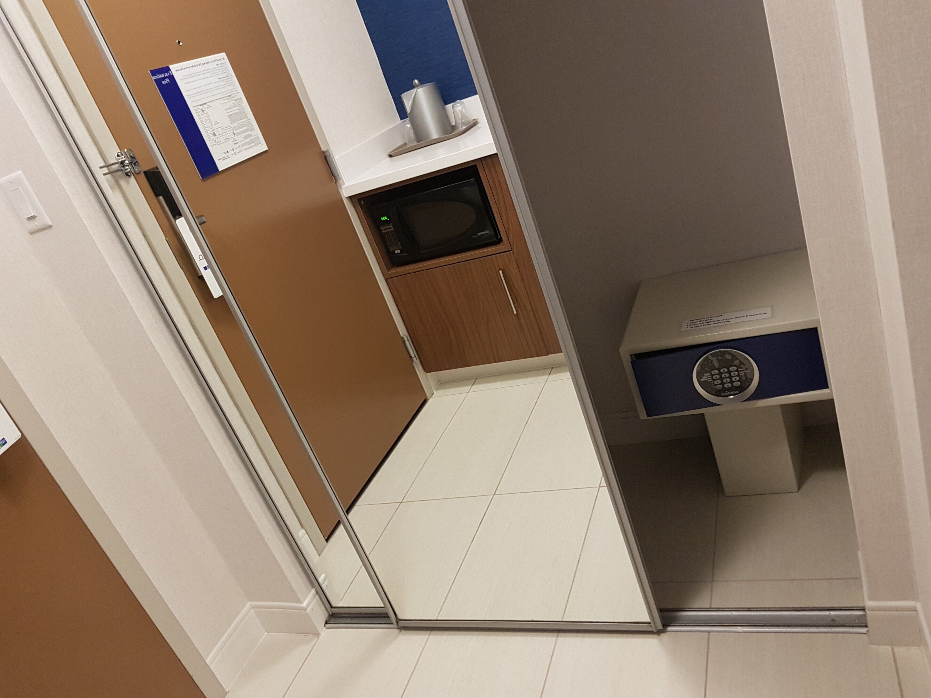 Un pasillo estrecho con un microondas, un mueble pequeño y un dispositivo azul en una estantería.
