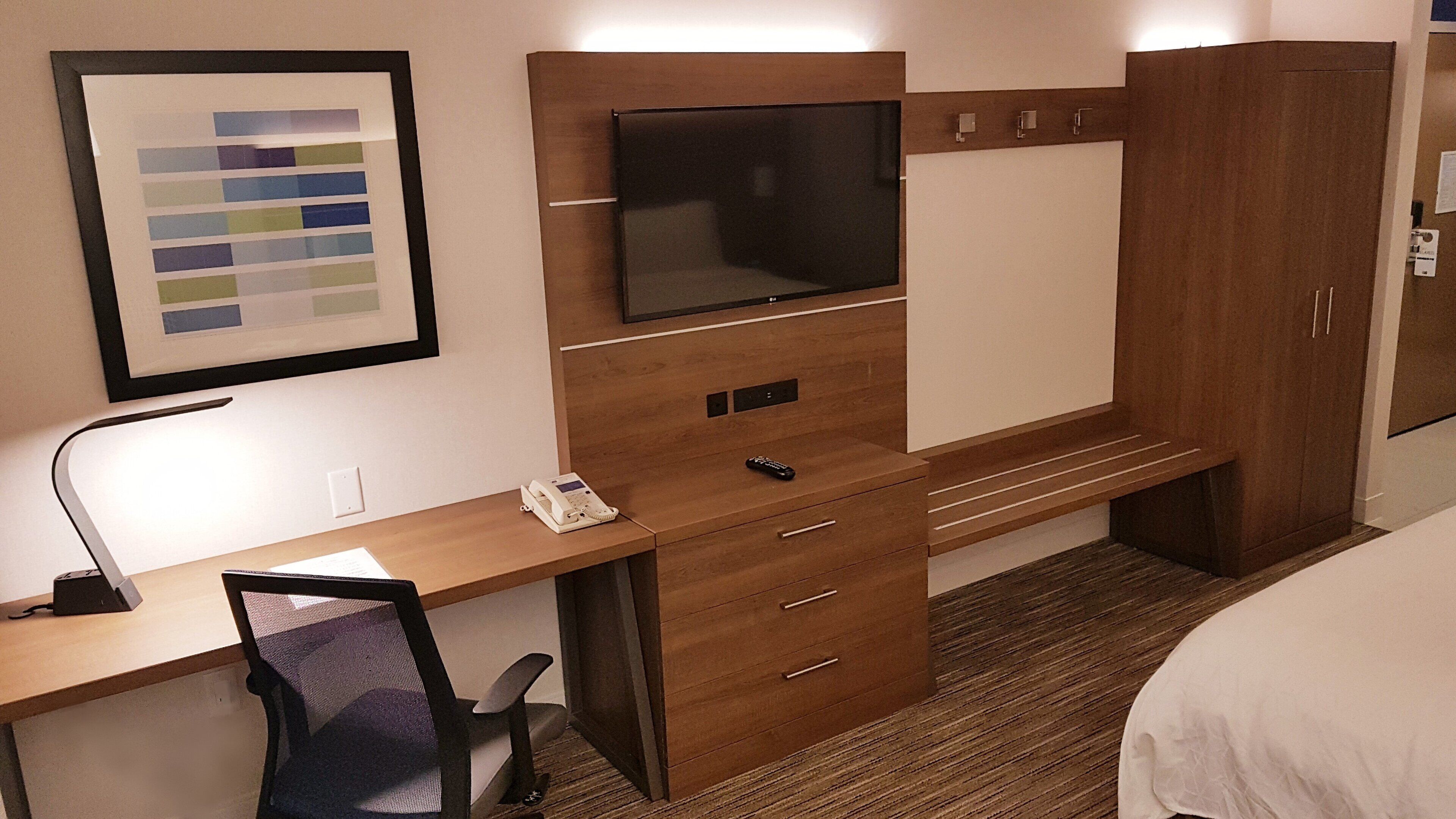 A hotel room with a wooden desk, a television, a telephone, and a framed picture on the wall.