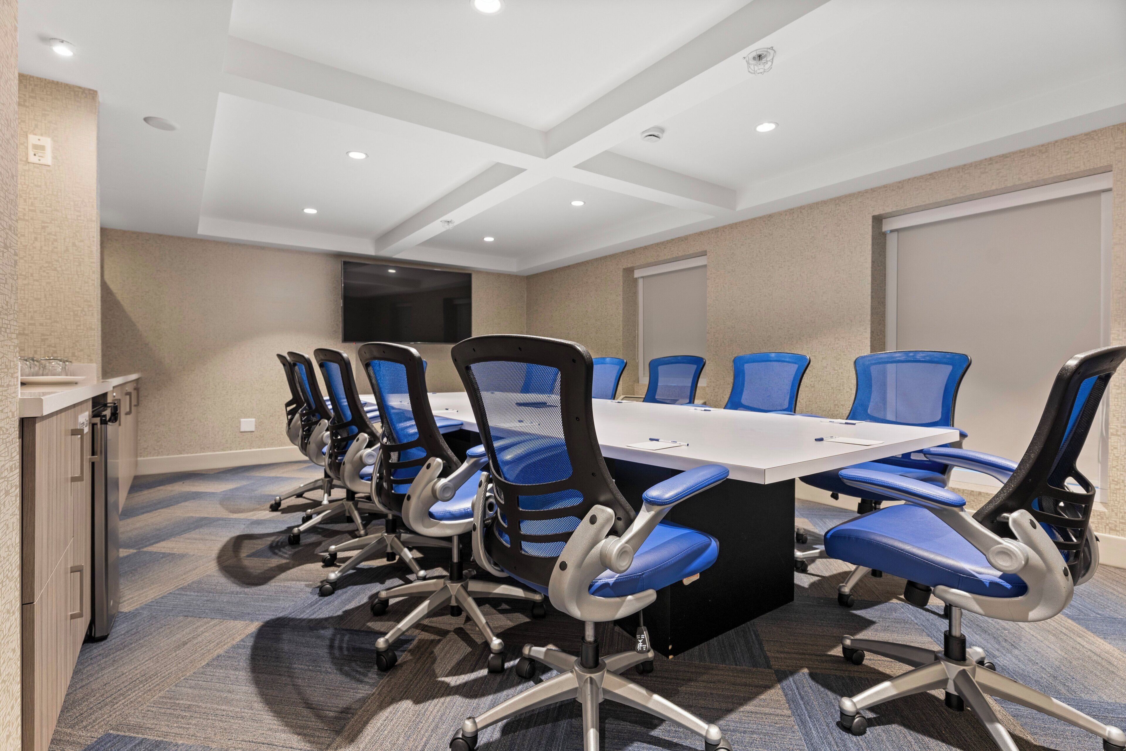 A conference room with a long table and blue chairs, equipped with wheels, in a modern hotel setting.