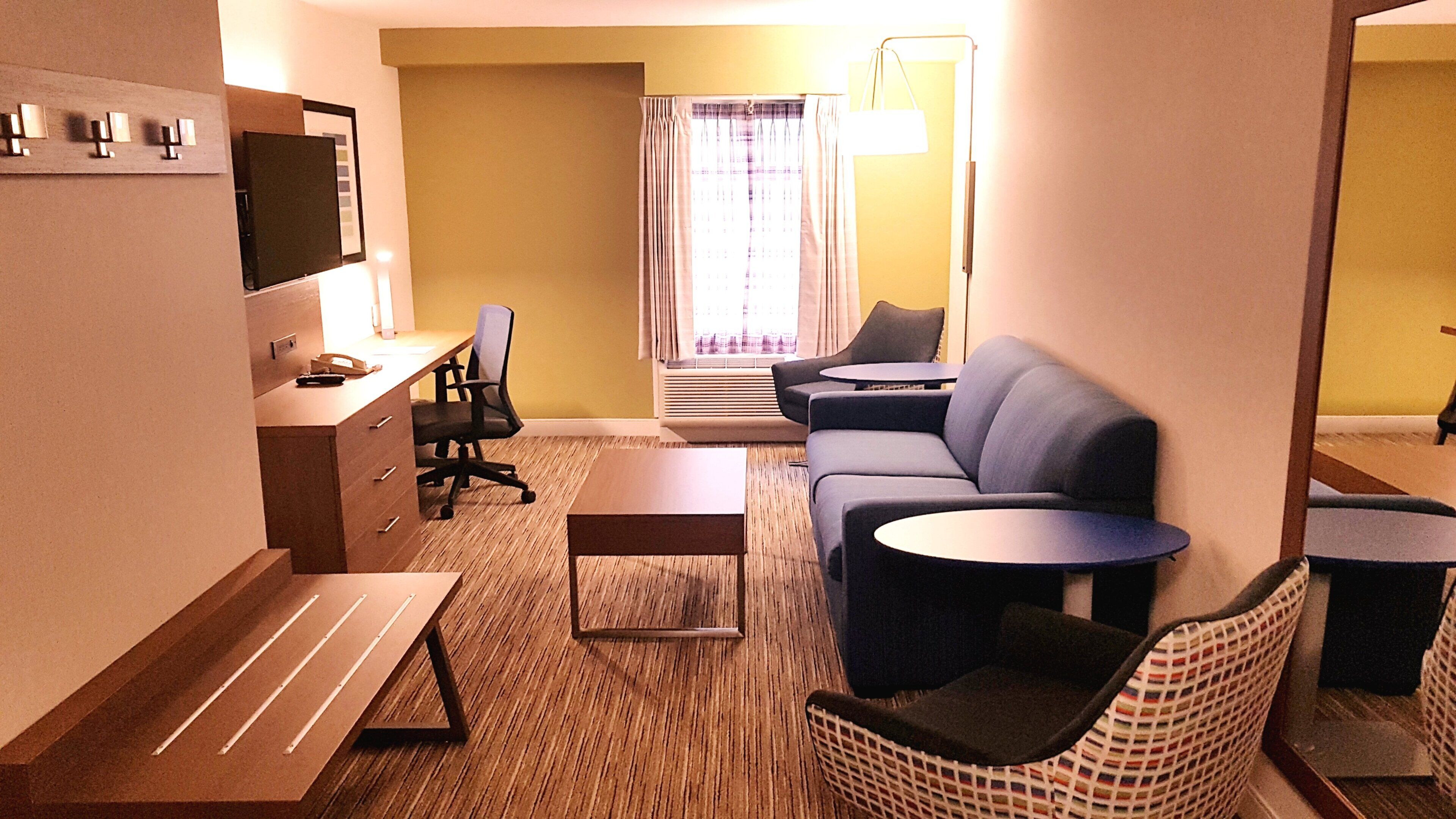 A hotel room with a sofa, a desk, a chair, a small table, and a lamp.