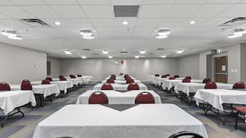 A conference room with rows of tables and chairs, equipped with ceiling lights and a fire extinguisher.