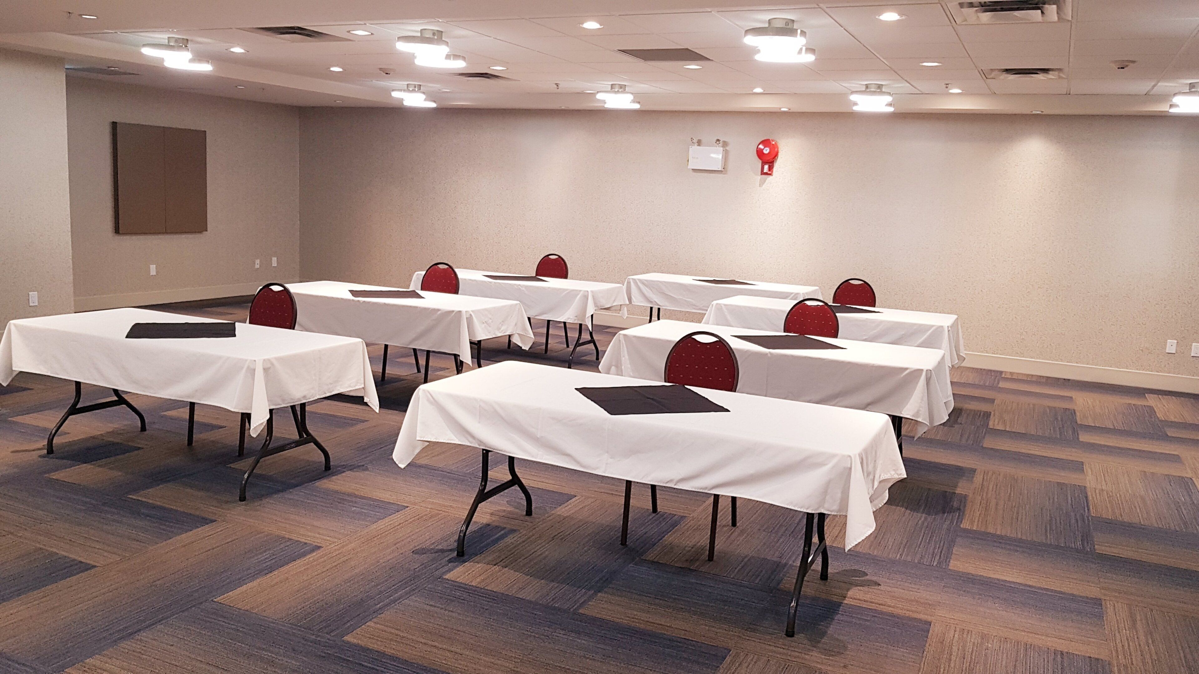 A conference room with multiple tables and chairs, equipped with ceiling lights and a fire alarm.
