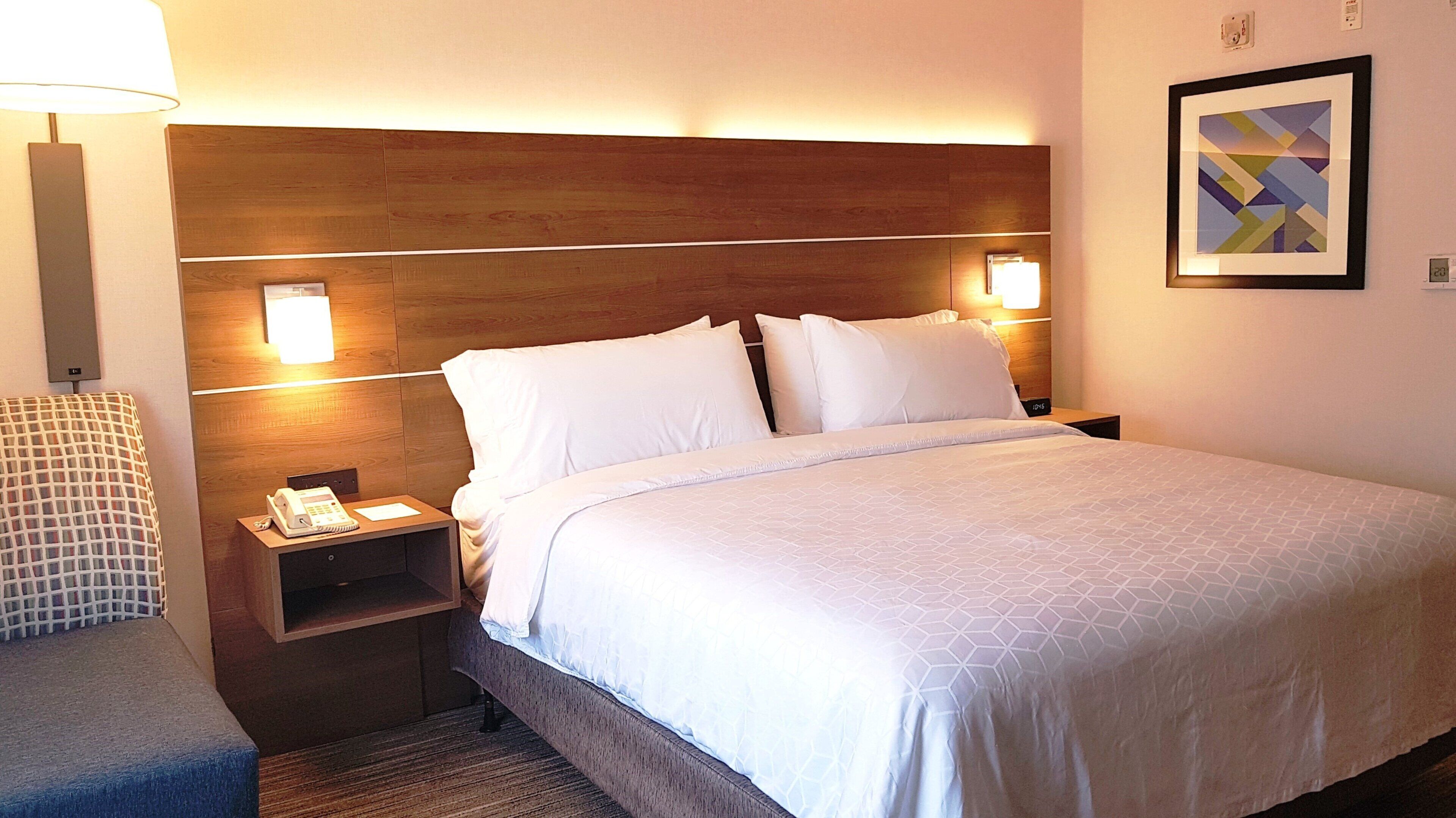 Una habitación de hotel con una cama grande, dos mesitas de noche, una lámpara y un cuadro enmarcado en la pared.