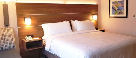 Una habitación de hotel con una cama grande, dos mesitas de noche, una lámpara y un cuadro enmarcado en la pared.